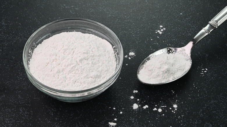 A bowl and spoon containing baking soda on a stone surface