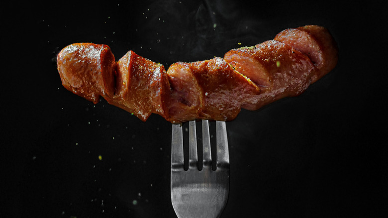 A fork holding a sizzling piece of sausage