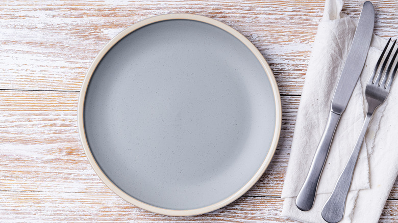 A place setting with a fork and knife on a napkin on a wood tabletop