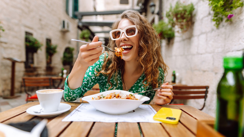 A person eating pasta at an outdoor table with sunglasses on