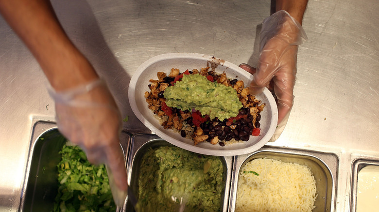 Chipotle employee scooping guacamole onto burrito bowl