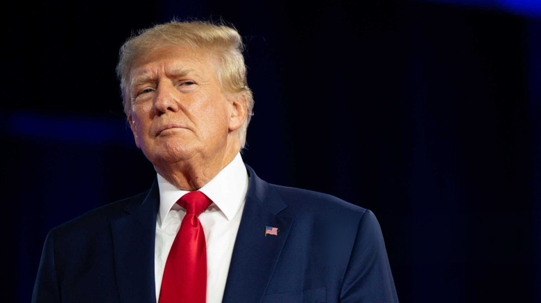 Donald Trump in a suit blue and red tie against a dark background.