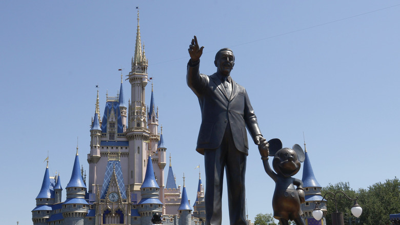 A statue of Walt Disney holding Mickey Mouse's hand in front of Cinderella's castle at Magic Kingdom, Disney World.