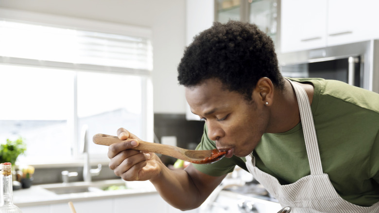 A young man tasting his food from a pot with a wooden spoon