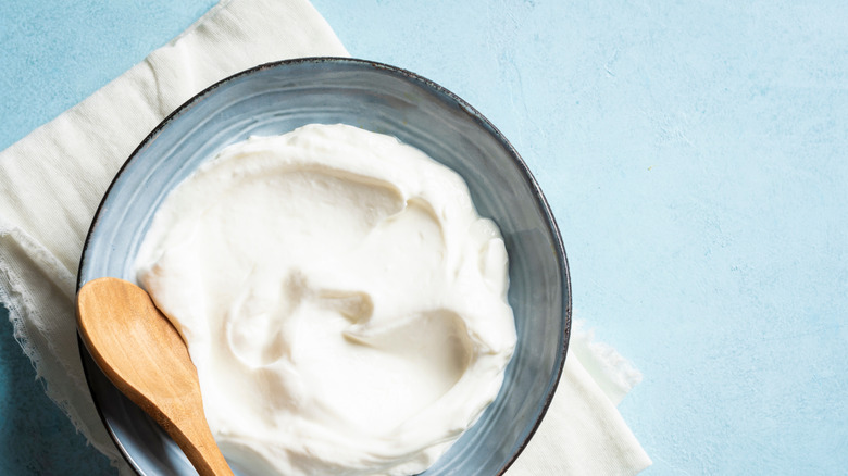 A bowl of cream on a table with a wooden spoon in the bowl