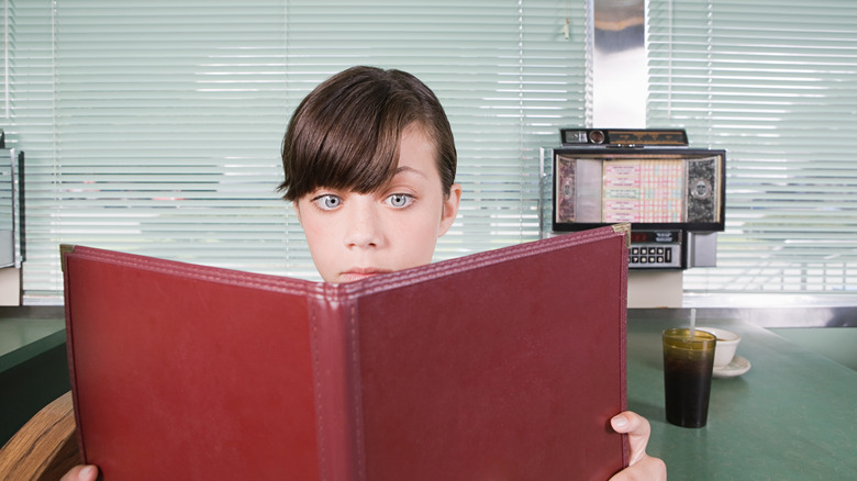 A person reading a large diner menu at a booth with a soda