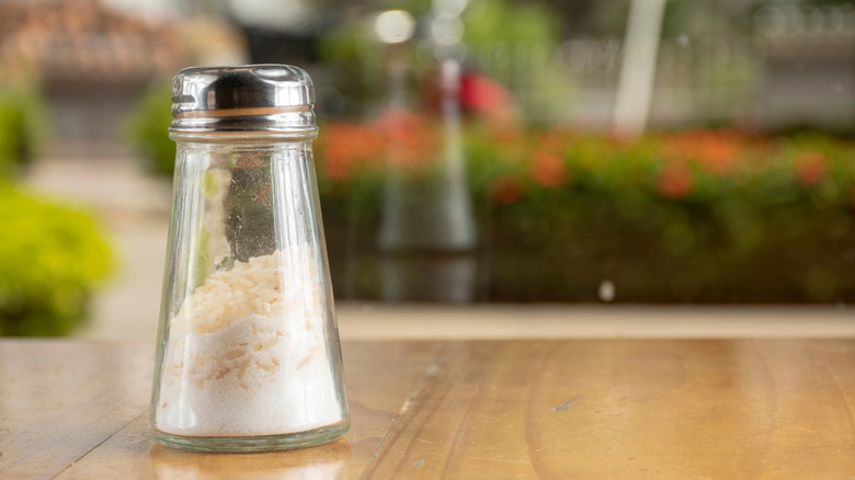 A salt shaker with rice on a wooden table