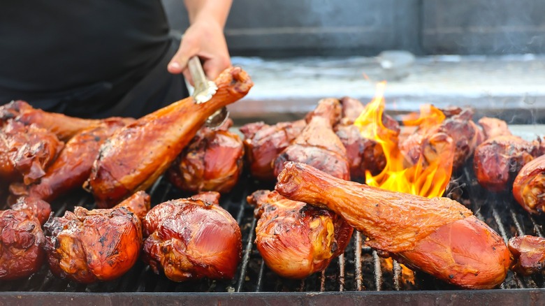 A person grilling turkey legs over a fire grate