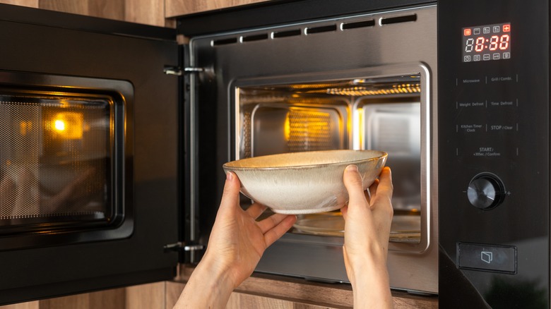 hands placing bowl in open microwave