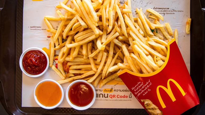 A large serving of McDonalds fries with several condiments, including ketchup