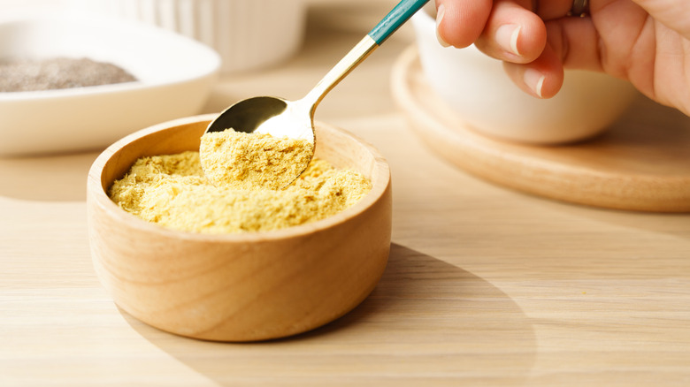 A spoon digging into nutritional yeast in wooden bowl.