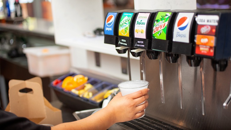 Person's hand holds a cup and uses a drink dispenser