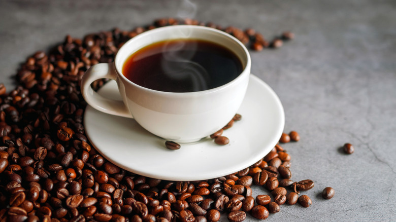 A cup of coffee and a saucer sitting on a cement surface.