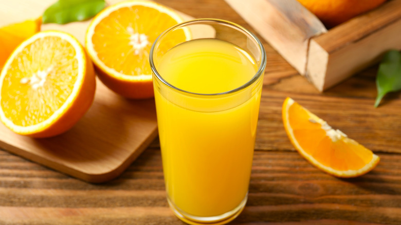 A glass of fresh orange juice beside slices of oranges on a cutting board