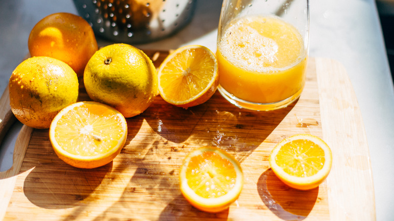 Squeezed orange juice slices on a cutting board with a glass of juice beside it.