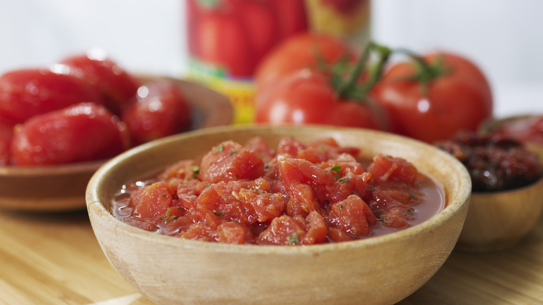 Canned diced tomato in a bowl with fresh tomatoes in the background