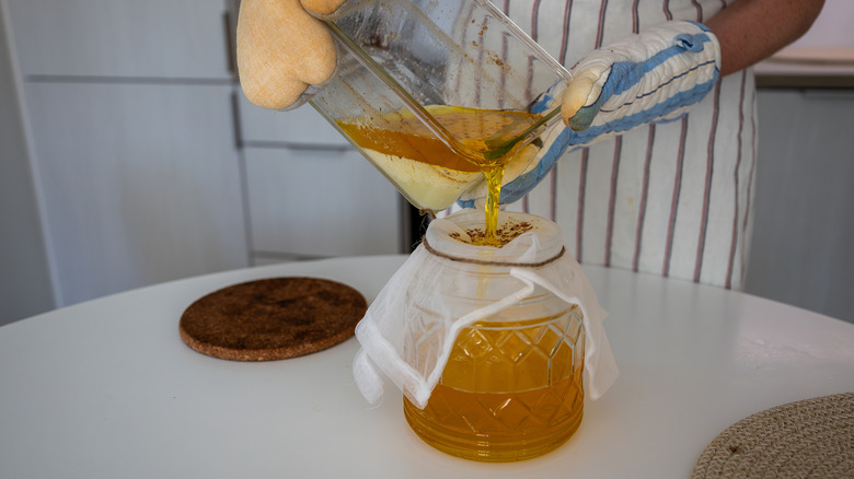 A person pouring ghee into glass jar through a straining cloth