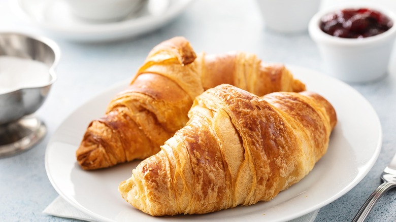 two croissants on a plate next to a ramekin of jelly