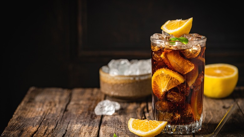 A cuba libre with ice and orange on a wooden table.