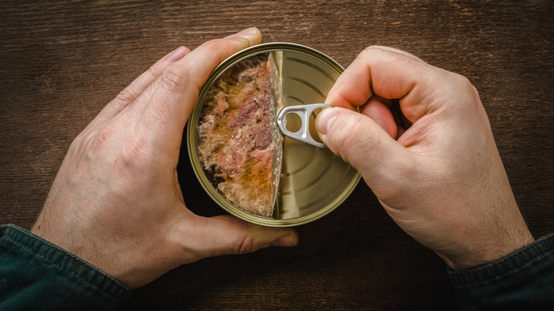 A person opening a can of chicken on a wooden table