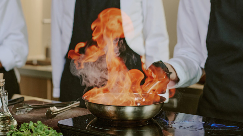 A chef holding a flaming skillet