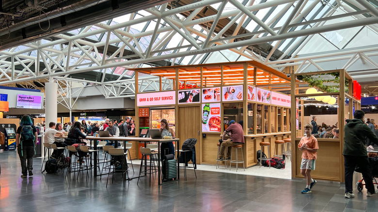 Exterior of an airport food court with tables and patrons