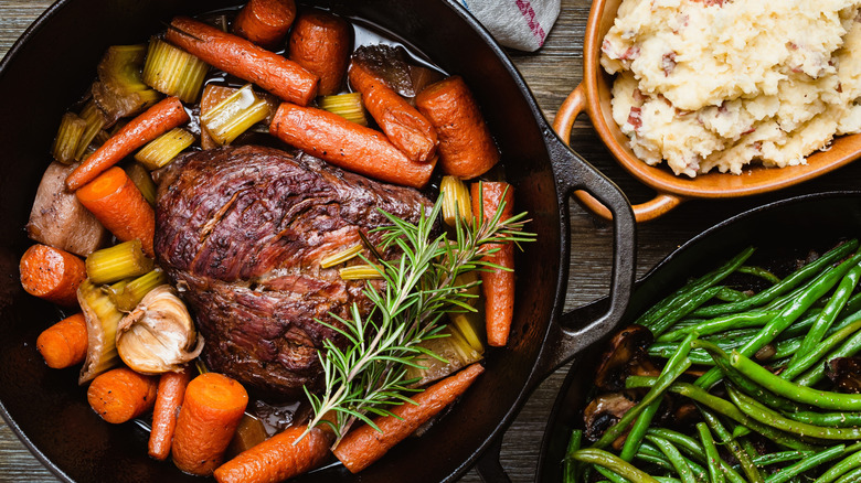 Pot roast and veggies in Dutch oven by mashed potatoes and green beans