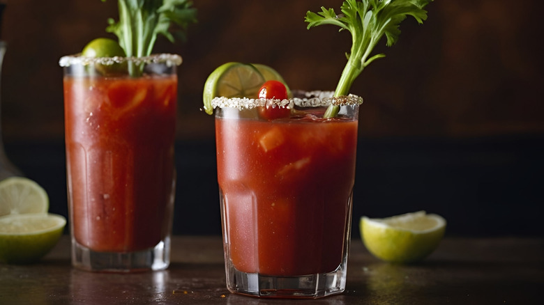 Two Bloody Mary cocktails with salted rims garnished with lime and celery