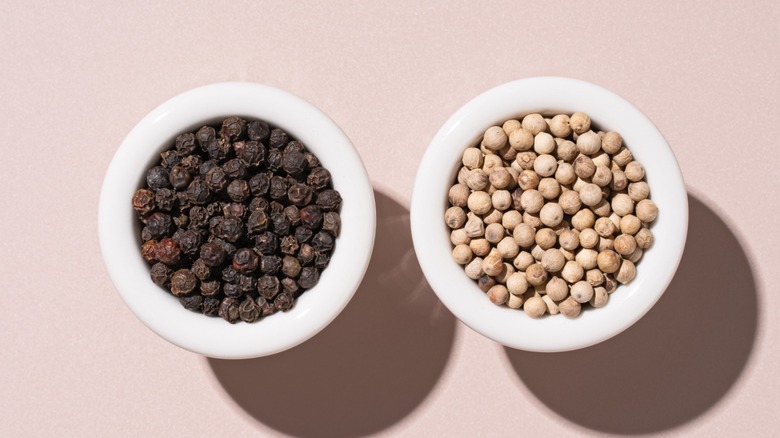 Two bowls side by side containing black peppercorns (left) and white peppercorns.