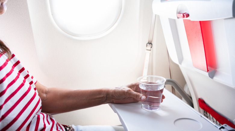 An airplane passenger holding a cup of water on their tray