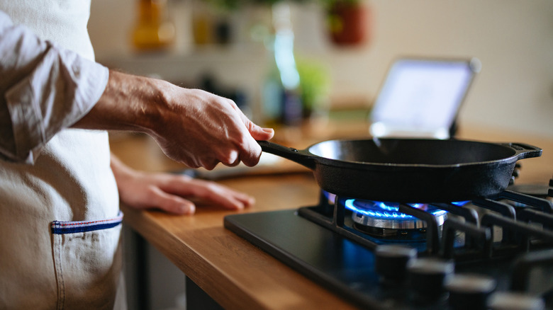 A person cooking with a cast iron skilled on lit gas stove