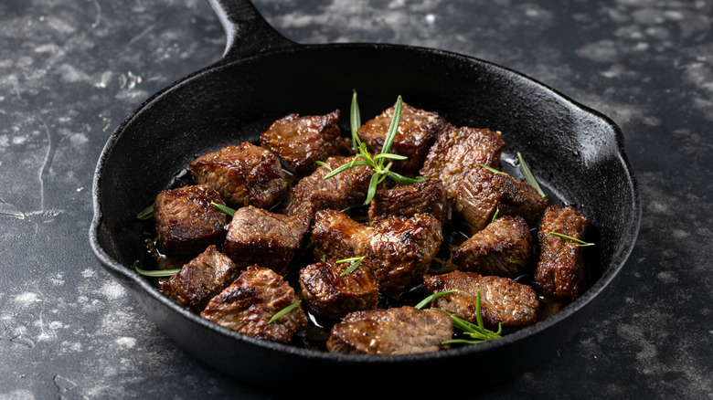 Cubed steak in a cast iron pan topped with fresh herbs