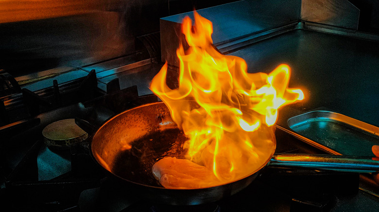 Skillet with chicken breasts on stovetop that has caught fire