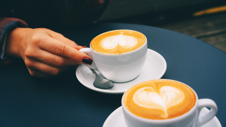 two cappuccinos on a table with hearts in the foam