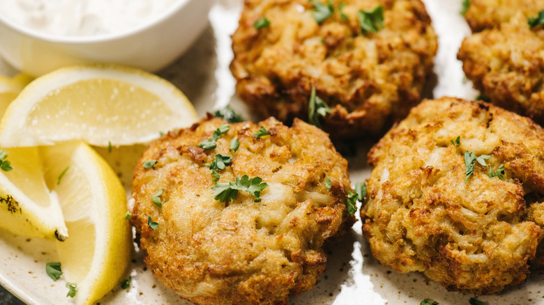 Crab cakes on a white plate with sliced lemons and tartar sauce