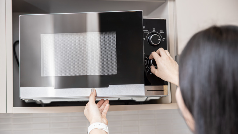 A woman adjusts the heat knob setting on an open microwave oven