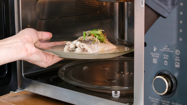 Hand removing plate of steamed fish from microwave