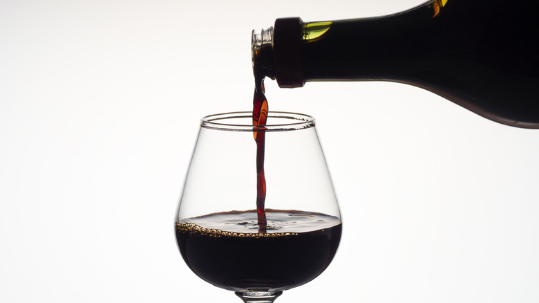 A bottle of red wine being poured into a glass