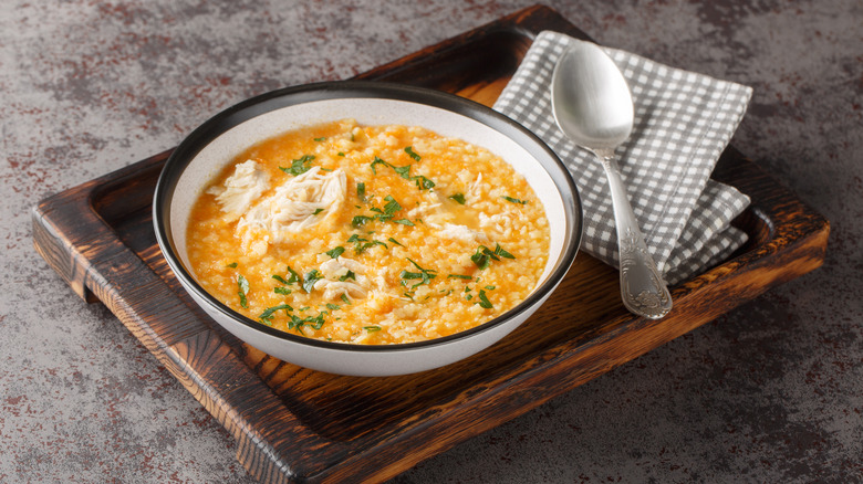 A bowl of pastina soup with chicken on a wooden serving tray