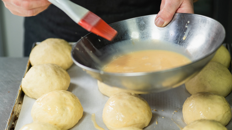 A baker brushing buns with egg wash