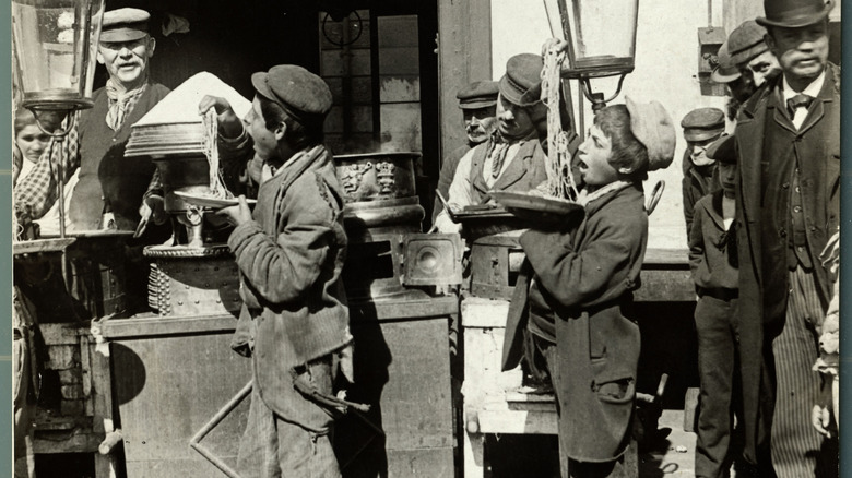 A black and white photo of boys eating spaghetti with their hands