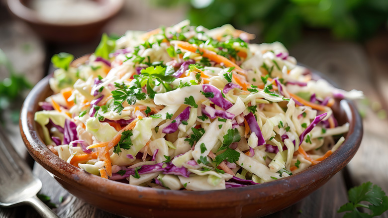 Coleslaw with green and red cabbage, shredded carrots, and herbs served in a brown bowl.