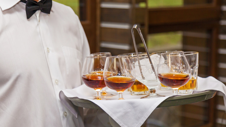 A formal waiter holding a tray of snifters filled with bourbon