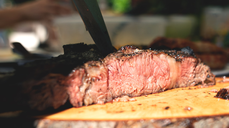 A knife cutting through a cooked slab of meat in partial sunlight