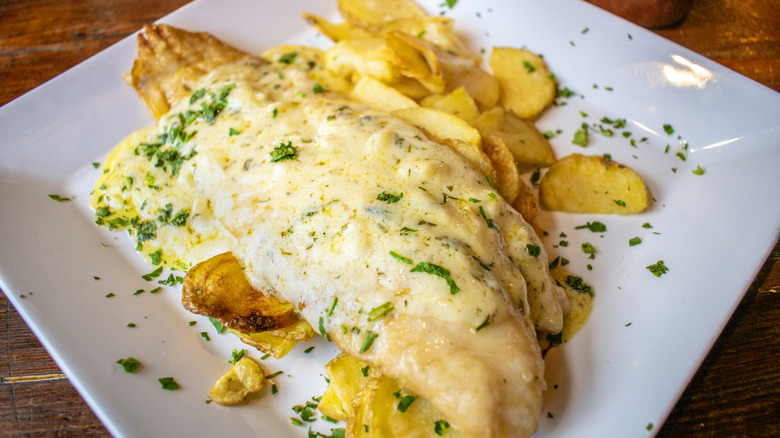 cheese melted over a fish fillet set atop potato chips on a white plate