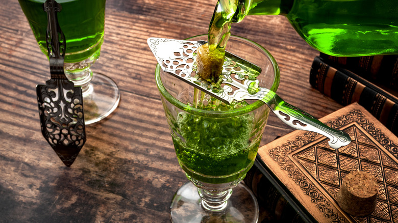 Pouring bottle of green-colored absinthe a over sugar cube into a glass