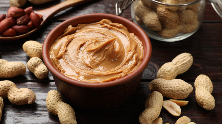 A bowl of peanut butter with whole and half peanuts surrounding it.