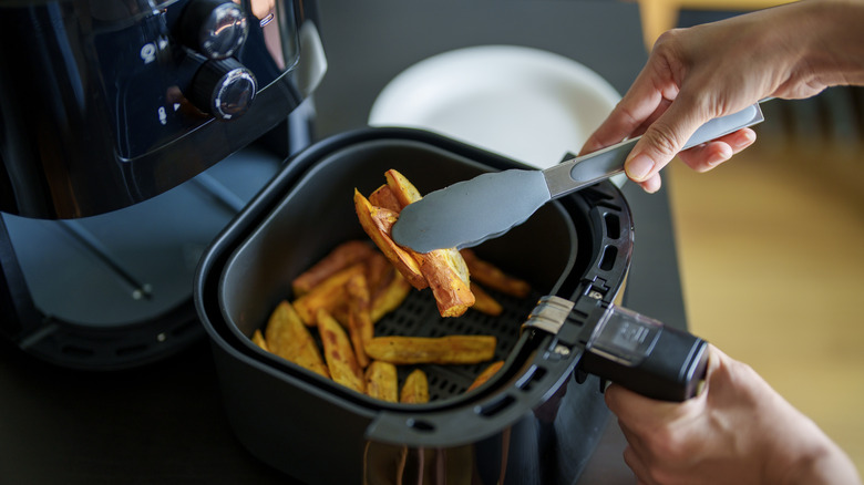 Person using silicone tongs to take fries out of air fryer