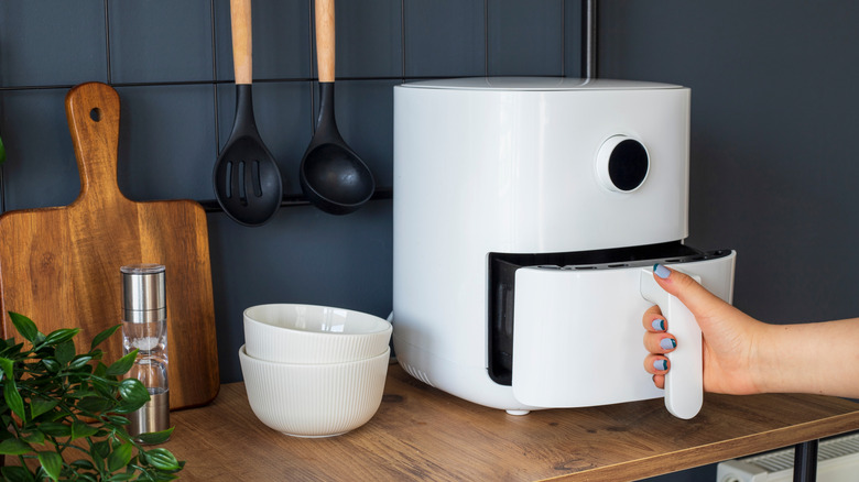 Person's hands opening a white air fryer on a kitchen counter