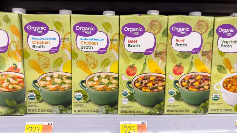 Cartons of chicken broth sit on a store shelf